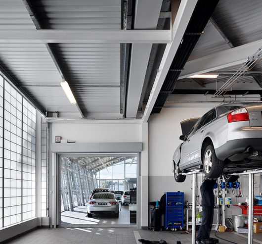 Man working on Audi suspended in air, with natural daylighting provided from a Kalwall facade as the backdrop