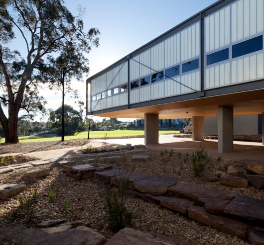 Exterior of building with Kalwall facade of unitized FRP wall panels on lifted columns surrounded by trees and rocks