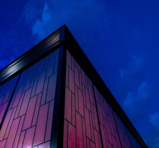 Upward angle of Dropzone project with Kalwall facade featuring pink backlighting against a dark blue sky.