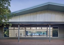 Community center exterior featuring tree and Kalwall facade w/ view to interior of building with people moving around inside.