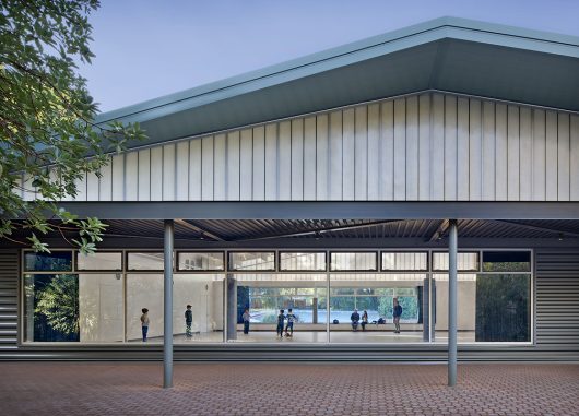 Community center exterior featuring tree and Kalwall facade w/ view to interior of building with people moving around inside.