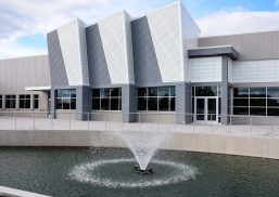 Magna Mirrors exterior featuring body of water with fountain and Kalwall-clad building facade.