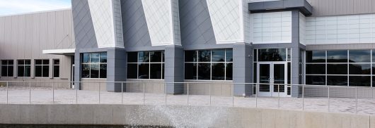 Magna Mirrors exterior featuring body of water with fountain and Kalwall-clad building facade.