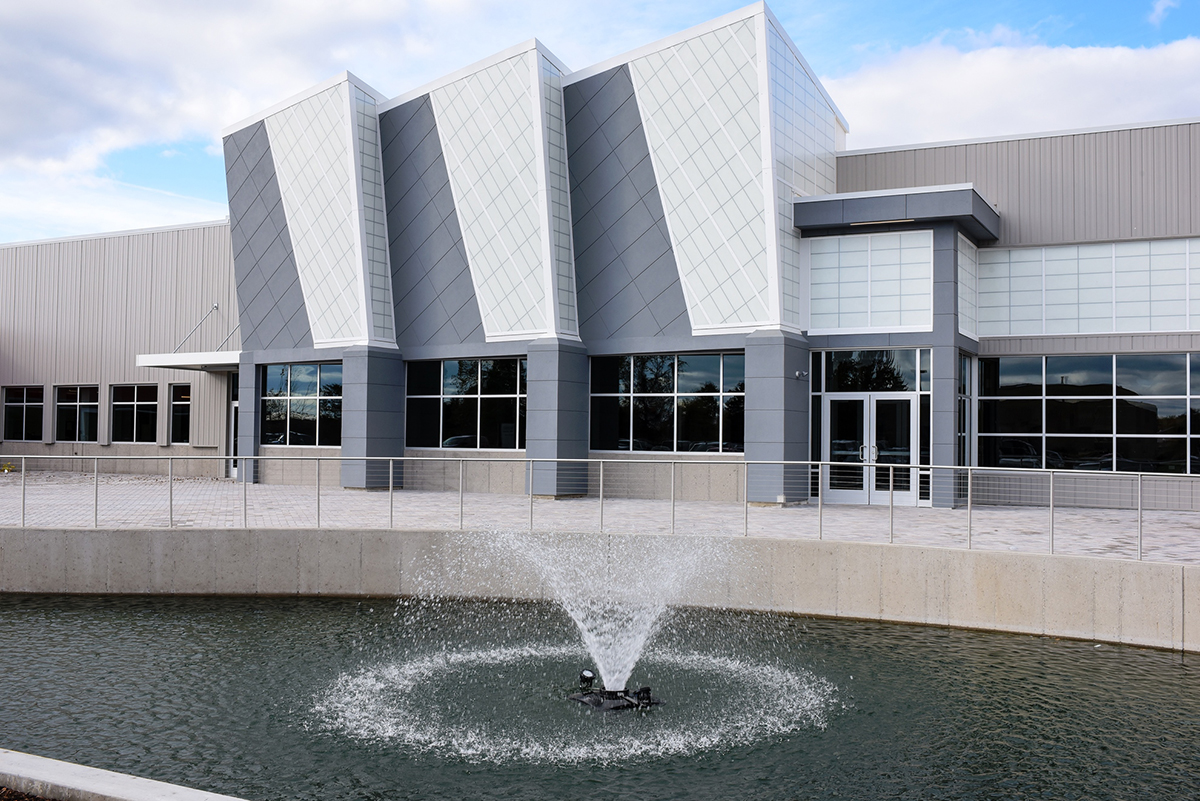 Magna Mirrors exterior featuring body of water with fountain and Kalwall-clad building facade.