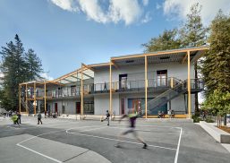 Exterior of school playground yard with concrete court with kids playing and gray building in background with Kalwall canopy.
