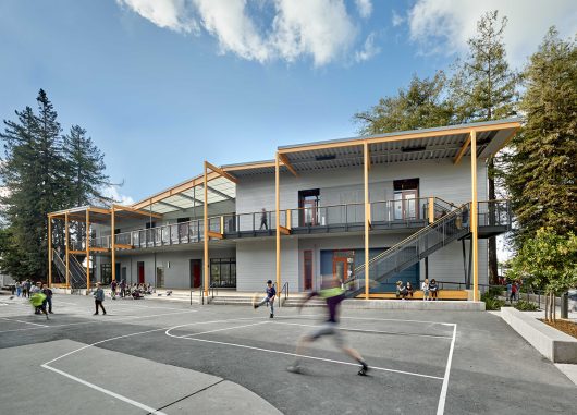 Exterior of school playground yard with concrete court with kids playing and gray building in background with Kalwall canopy.