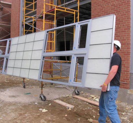 Two male construction workers carry a lightweight, unitized Kalwall panel to be installed on building