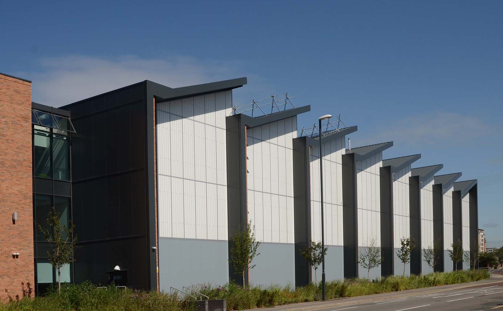 Leeds College exterior set amongst blue sky and green plants featuring Kalwall facades with sloped roofs.