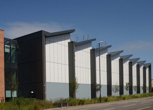 Leeds College exterior set amongst blue sky and green plants featuring Kalwall facades with sloped roofs.