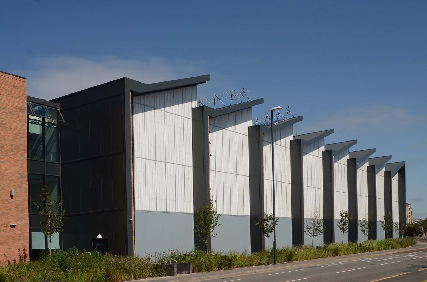 Leeds College exterior set amongst blue sky and green plants featuring Kalwall facades with sloped roofs.