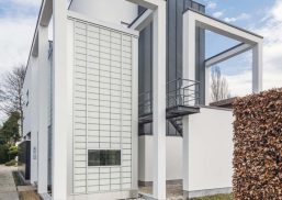 White metal-framed building featuring Kalwall facade with glimpses of trees and blue sky with slight clouds.