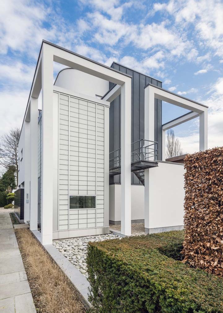 White metal-framed building featuring Kalwall facade with glimpses of trees and blue sky with slight clouds.