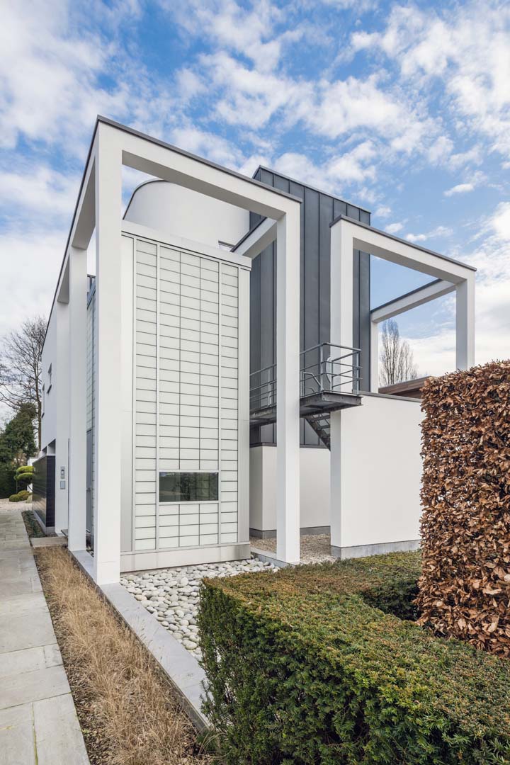 White metal-framed building featuring Kalwall facade with glimpses of trees and blue sky with slight clouds.