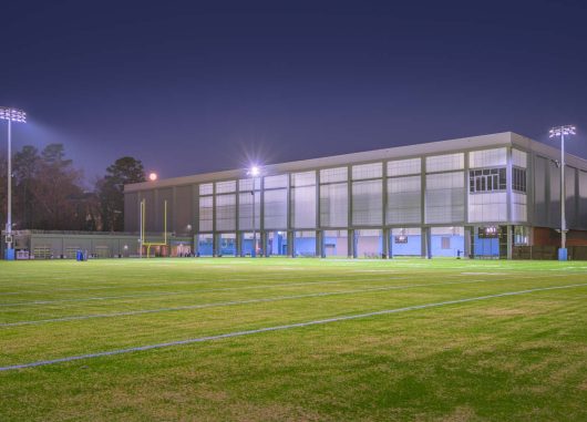 UNC football field at nighttime with building in the background featuring Kalwall facade.