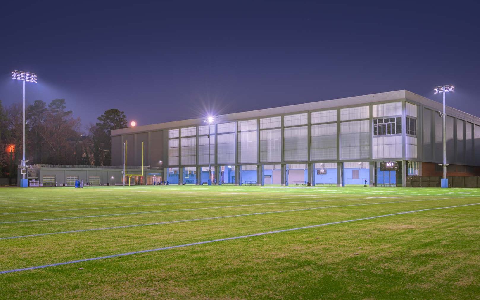 UNC football field at nighttime with building in the background featuring Kalwall facade.