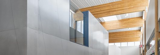Interior of school with children walking among metal walls and wooden beams underneath Kalwall skylight system