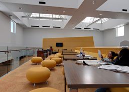 Students working at wooden tables with yellow furniture surrounding them and Kalwall skylights providing overhead daylight