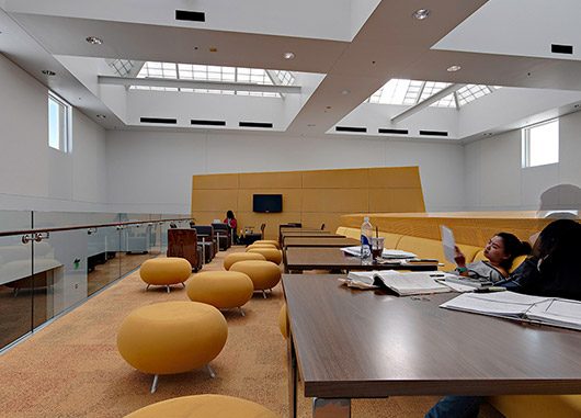 Students working at wooden tables with yellow furniture surrounding them and Kalwall skylights providing overhead daylight