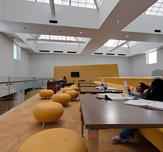 Students working at wooden tables with yellow furniture surrounding them and Kalwall skylights providing overhead daylight