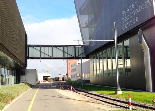 Nestle building featuring a Kalwall walkway above a road with green grass and connecting two buildings