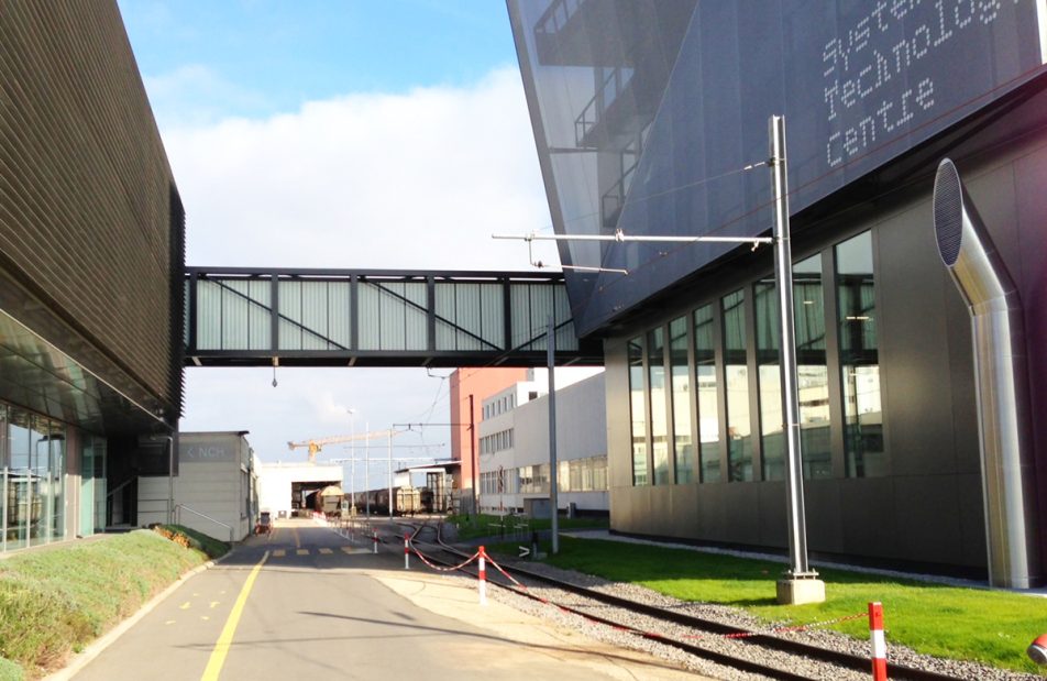 Nestle building featuring a Kalwall walkway above a road with green grass and connecting two buildings