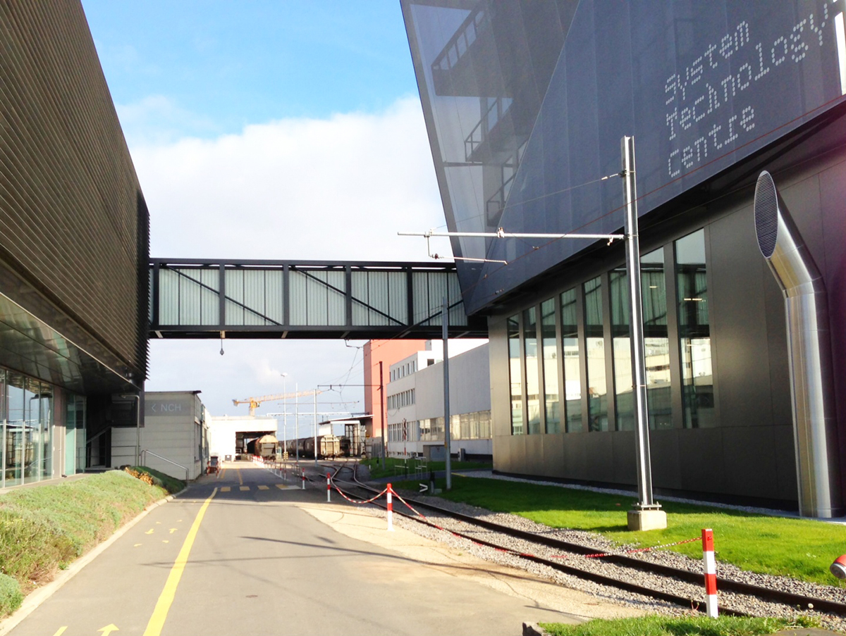 Nestle building featuring a Kalwall walkway above a road with green grass and connecting two buildings