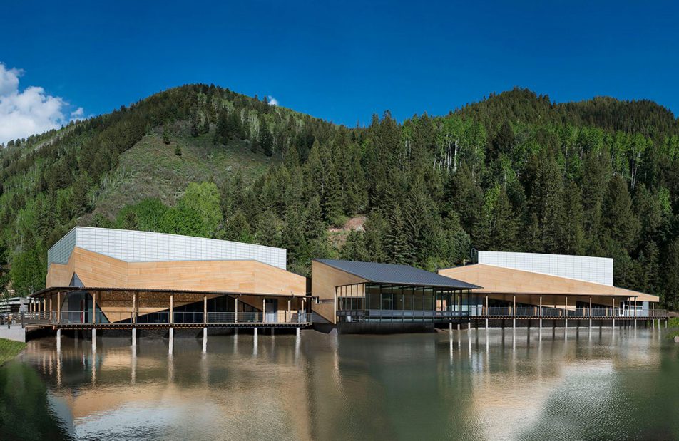 Exterior of Aspen Music School featuring building covered in a Kalwall facade surrounded by water and mountains with trees