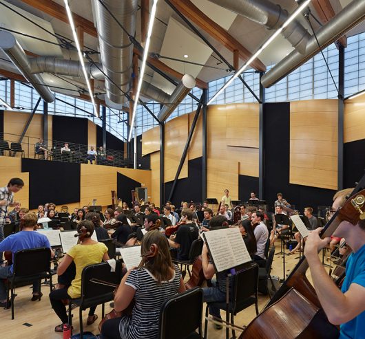 Interior of Aspen Music School shows students playing instruments in orchestra rehearsal with Kalwall facade on upper walls