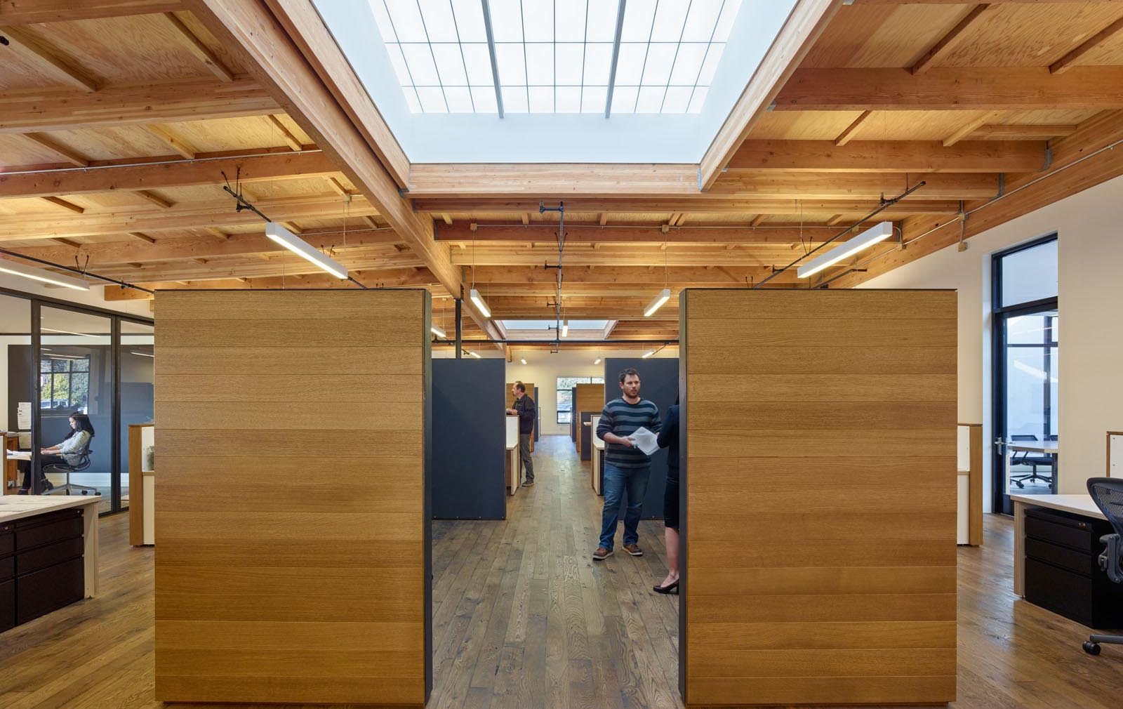 1060 Redwood office building interior with people standing among wooden walls, desks, and Kalwall translucent skylights above