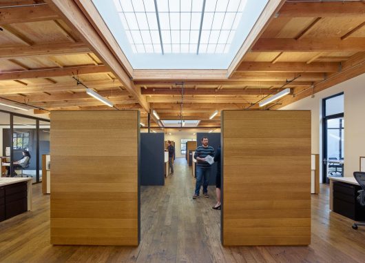 1060 Redwood office building interior with people standing among wooden walls, desks, and Kalwall translucent skylights above
