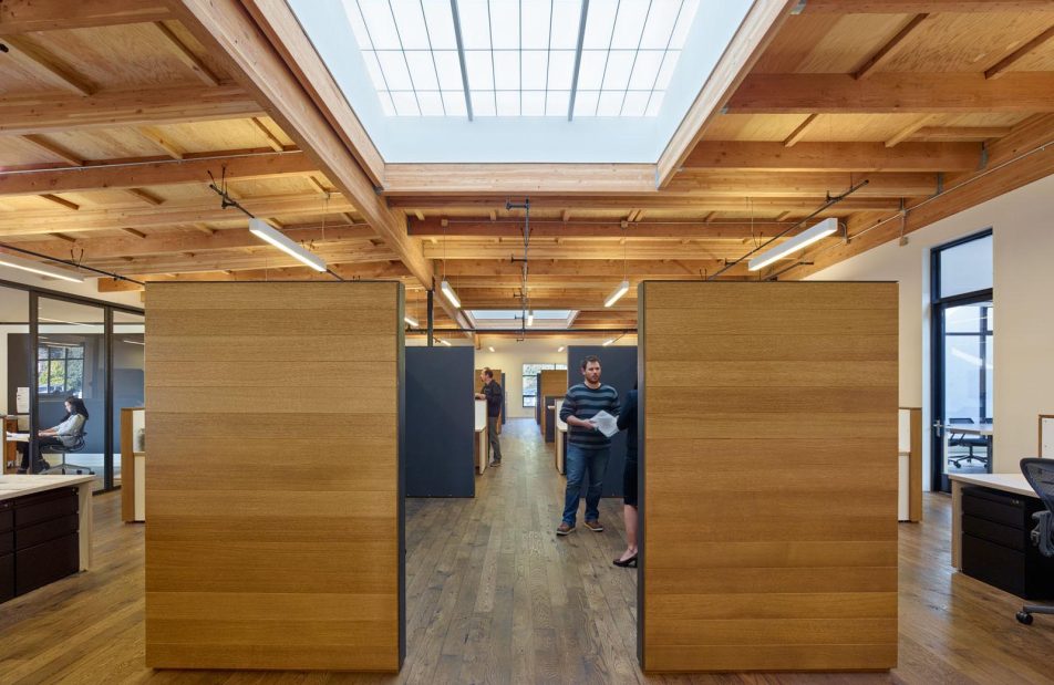 1060 Redwood office building interior with people standing among wooden walls, desks, and Kalwall translucent skylights above