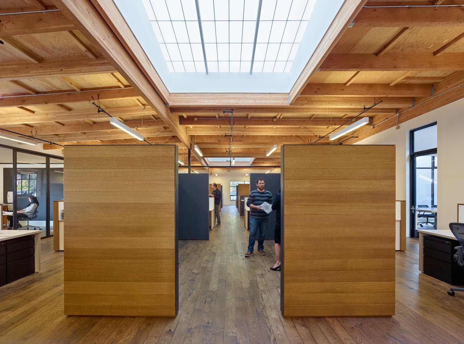 1060 Redwood office building interior with people standing among wooden walls, desks, and Kalwall translucent skylights above