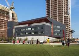 High school exterior with Kalwall curtain wall facade with kids playing soccer in foreground and two buildings in background