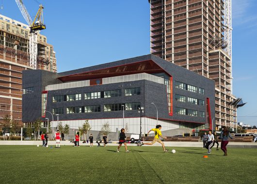 High school exterior with Kalwall curtain wall facade with kids playing soccer in foreground and two buildings in background