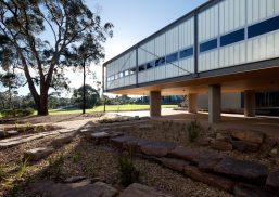 Exterior of building with Kalwall facade of unitized FRP wall panels on lifted columns surrounded by trees and rocks