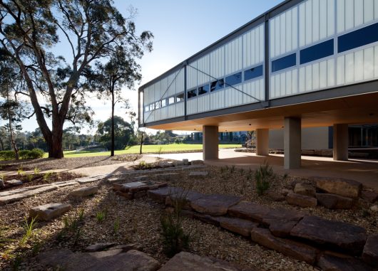 Exterior of building with Kalwall facade of unitized FRP wall panels on lifted columns surrounded by trees and rocks