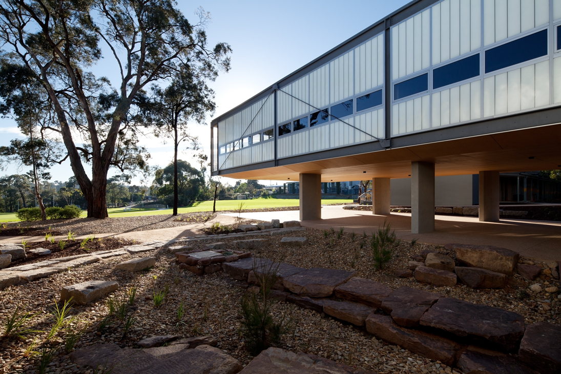 Exterior of building with Kalwall facade of unitized FRP wall panels on lifted columns surrounded by trees and rocks