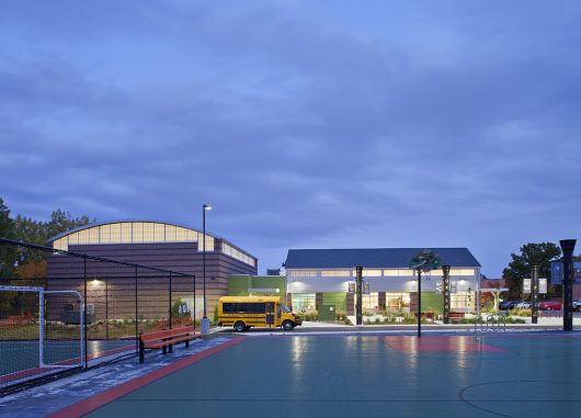 Boys & Girls Club exterior at nighttime featuring building with backlit Kalwall curtain wall system and school bus out front