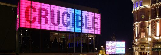 Crucible Theater building exterior with glass walls and sign with large lettering on Kalwall facade featuring backlighting