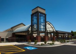 Healthcare center exterior set amongst blue sky in a parking lot with Kalwall canopy and glass column on building
