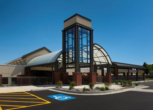 Healthcare center exterior set amongst blue sky in a parking lot with Kalwall canopy and glass column on building