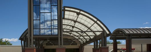 Translucent canopy entrance of Johnson County Healthcare Center, featuring modern architectural design, large glass panels, and a curved roof structure, enhancing daylighting and aesthetic appeal.
