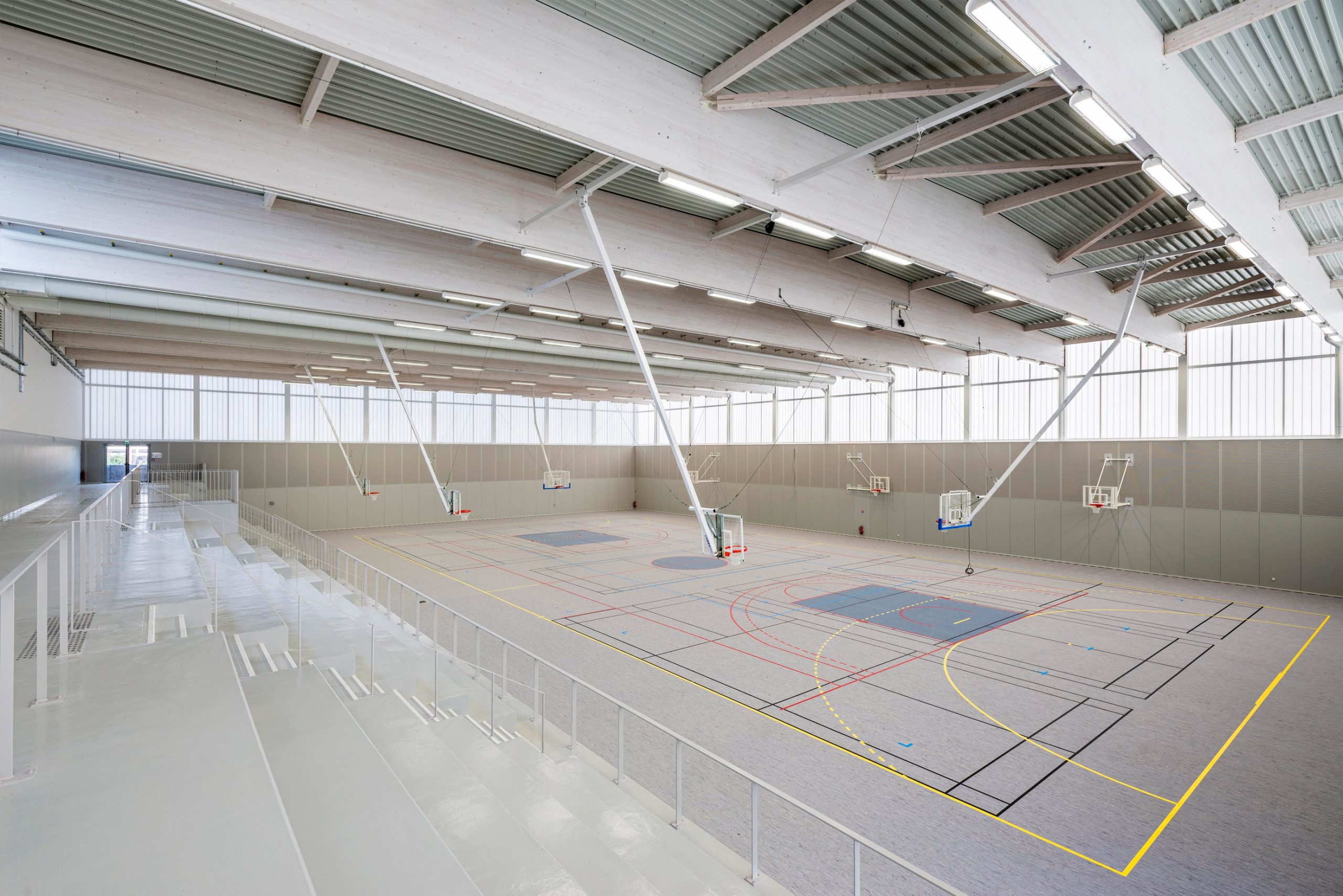 Minimalistic interior of Complexe Sportif featuring three basketball hoops in space with translucent wall panels from Kawall