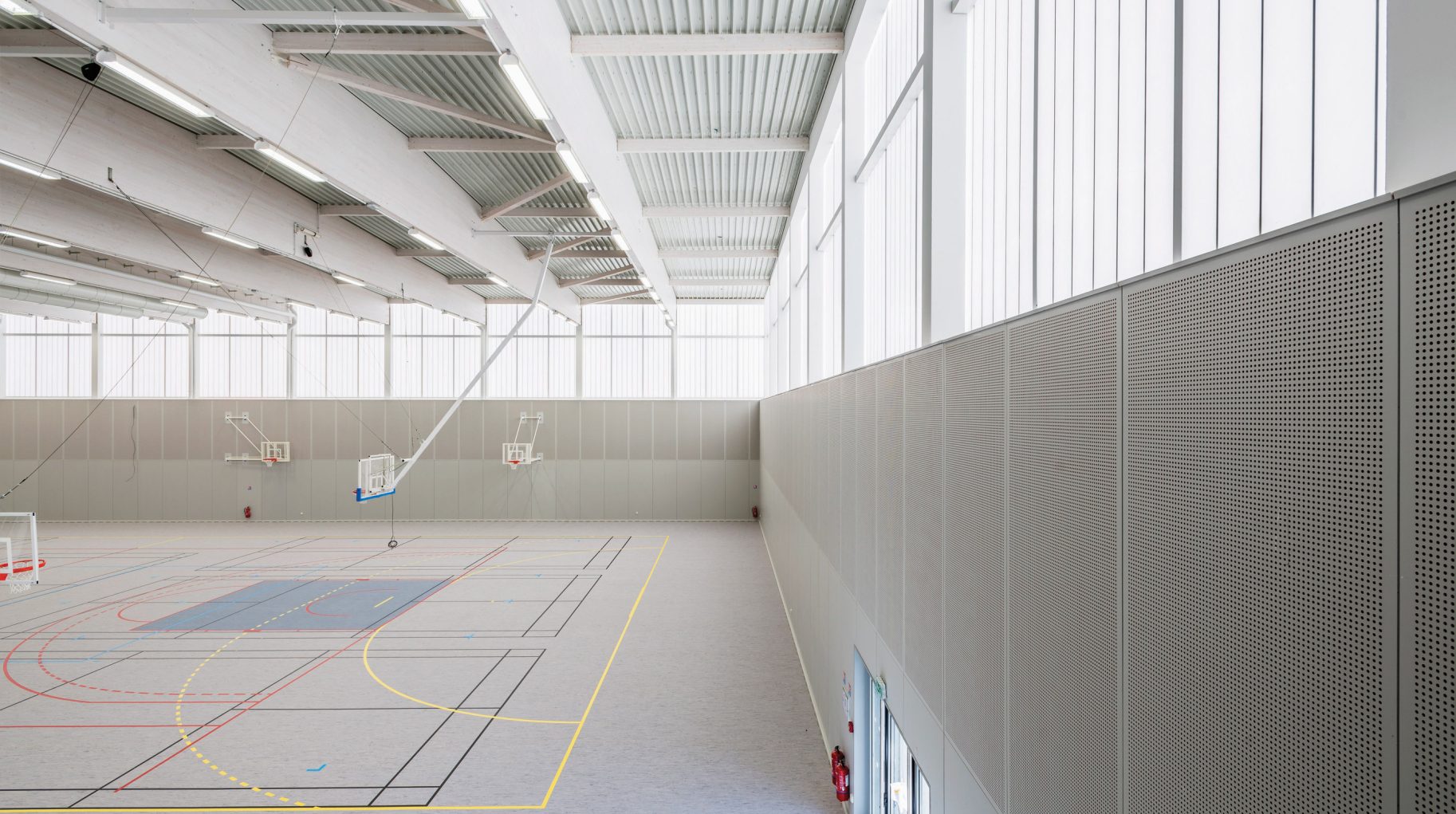 Minimalistic interior of Complexe Sportif featuring three basketball hoops in space with translucent wall panels from Kawall