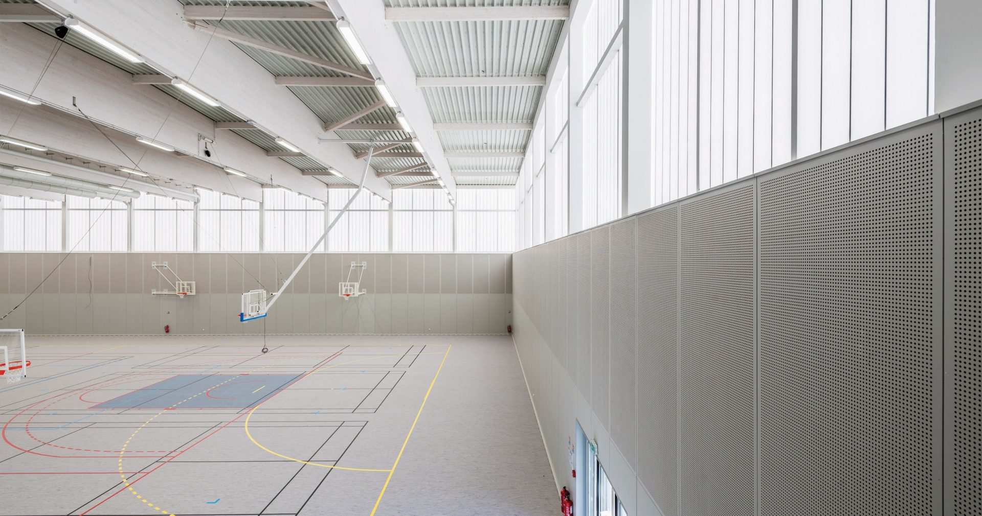 Minimalistic interior of Complexe Sportif featuring three basketball hoops in space with translucent wall panels from Kawall