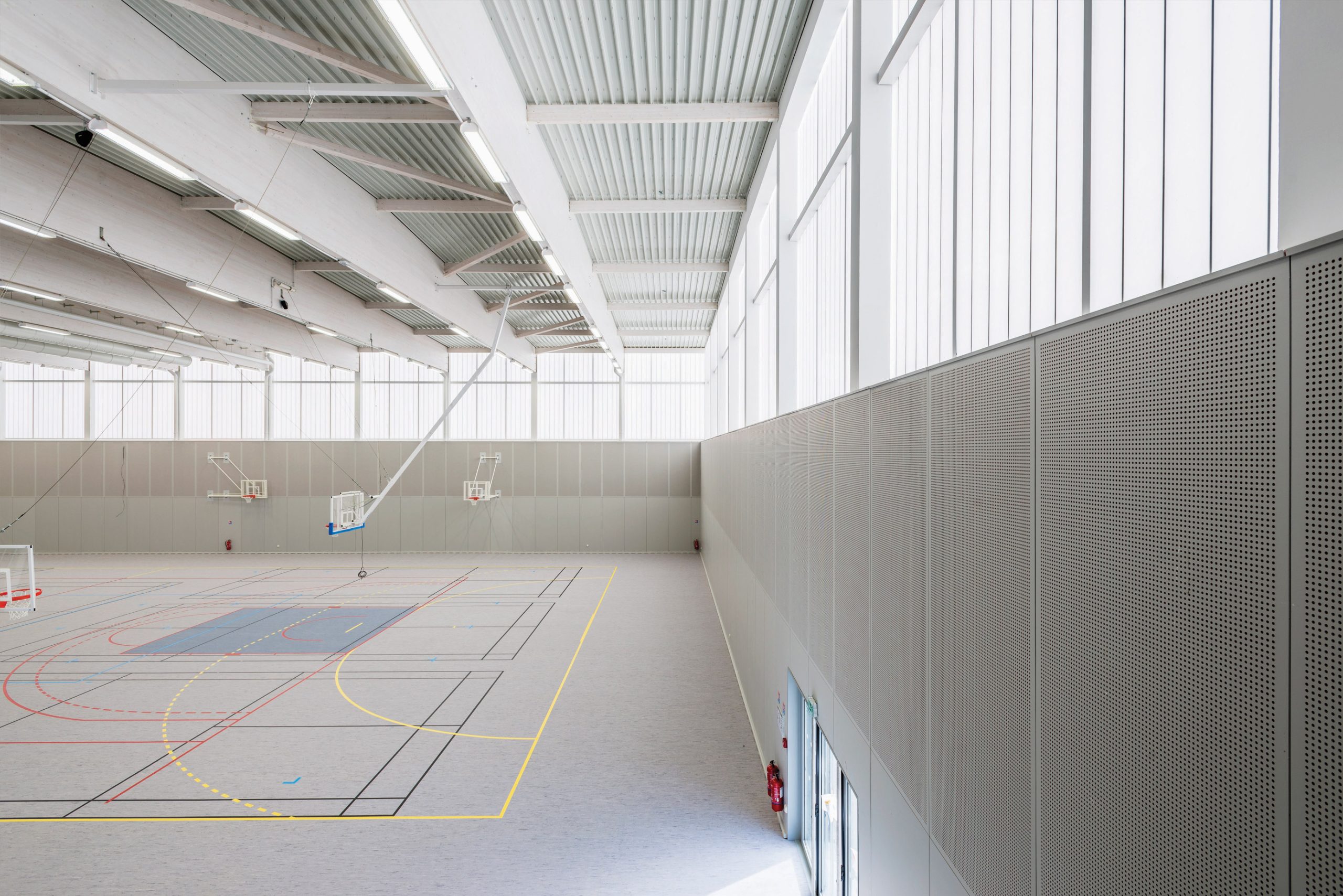 Minimalistic interior of Complexe Sportif featuring three basketball hoops in space with translucent wall panels from Kawall