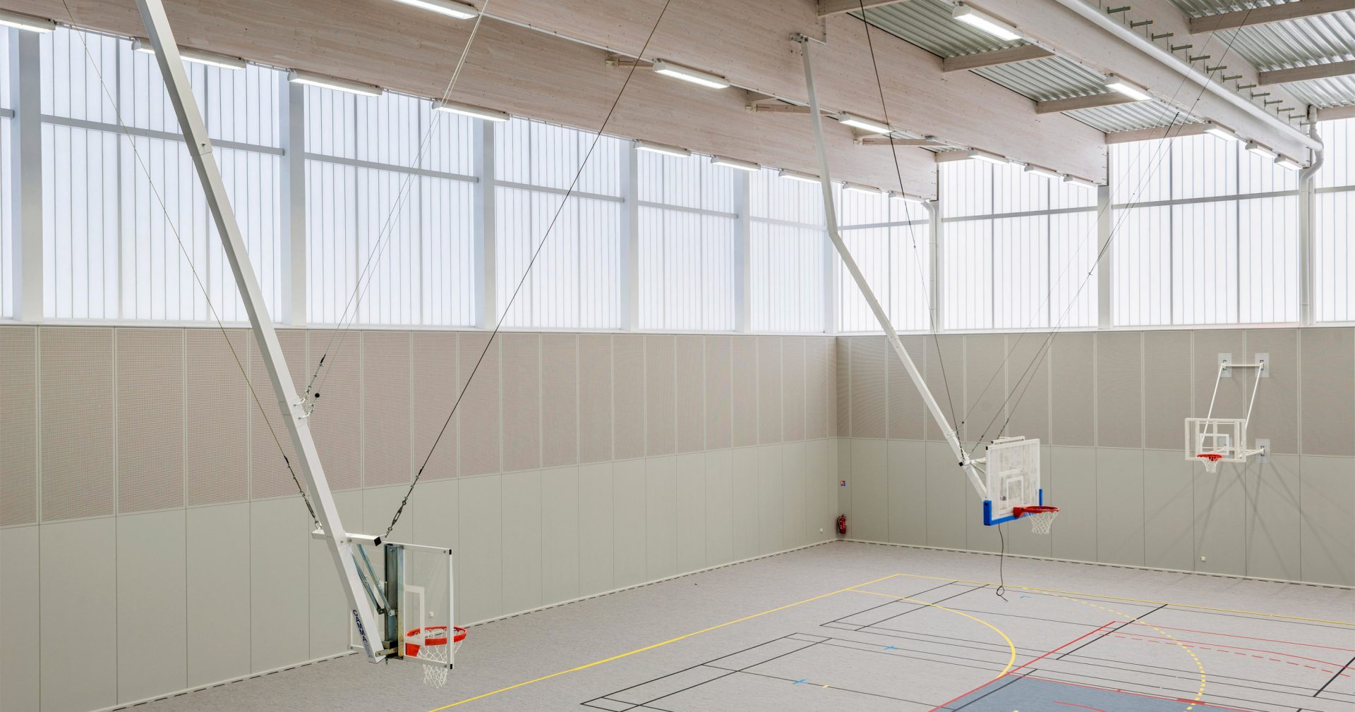 Minimalistic interior of Complexe Sportif featuring three basketball hoops in space with translucent wall panels from Kawall