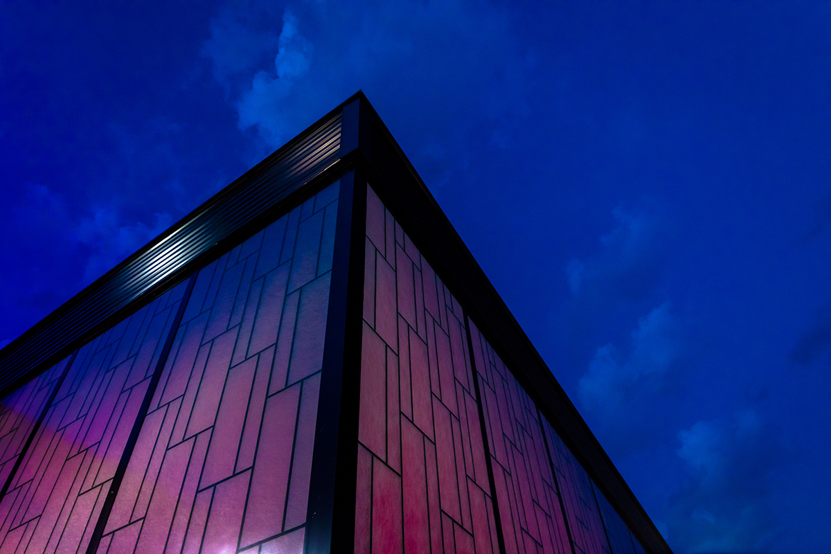 Upward angle of Dropzone project with Kalwall facade featuring pink backlighting against a dark blue sky.