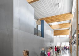 Interior of school with children walking among metal walls and wooden beams underneath Kalwall skylight system