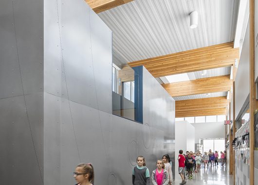 Interior of school with children walking among metal walls and wooden beams underneath Kalwall skylight system